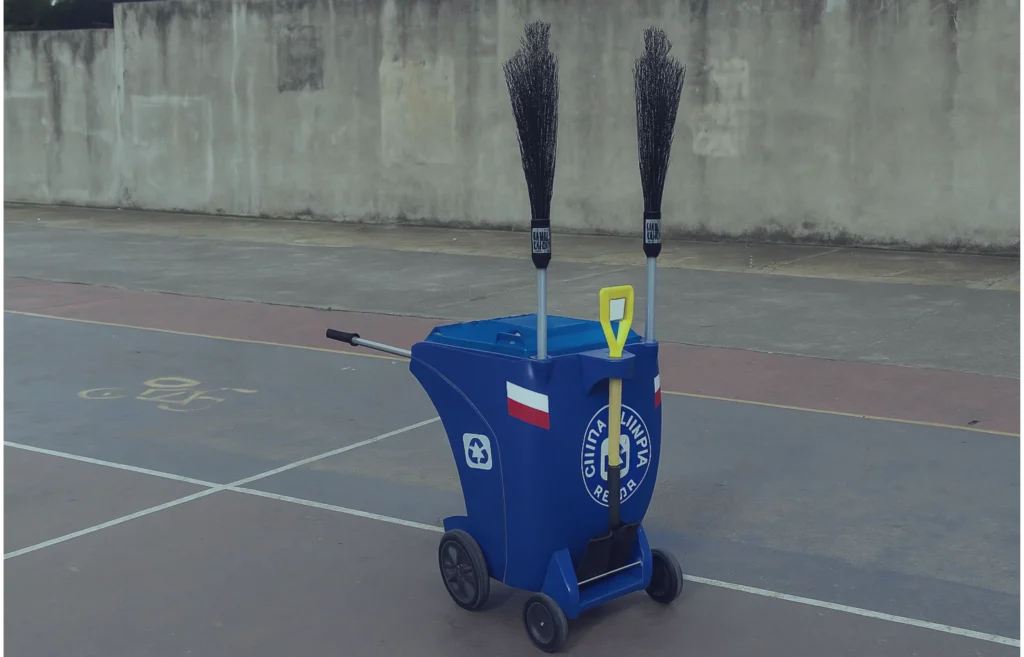 Carro barrendero azul con pala y escobas, diseñado para limpieza vial en canchas y espacios deportivos al aire libre.